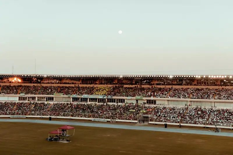 Crowded stadium stands under a clear evening sky with the moon rising