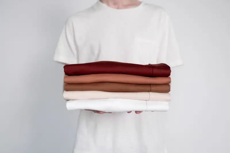 Hands holding a neat stack of folded t-shirts in warm neutral colors