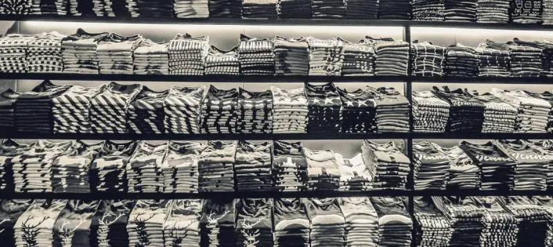 Black and white view of shelves stacked with folded t-shirts in a store