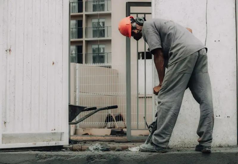 Worker in an orange hard hat breaking concrete with a jackhammer on a city site