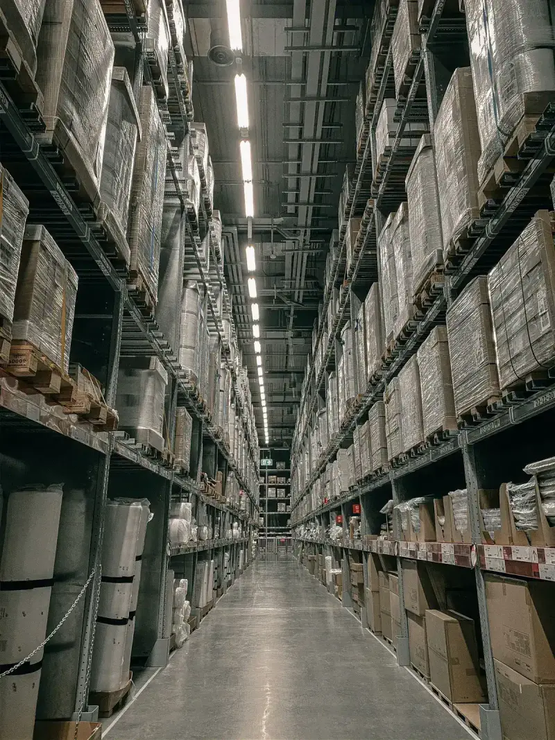 Long warehouse aisle lined with tall shelving stocked with boxed goods
