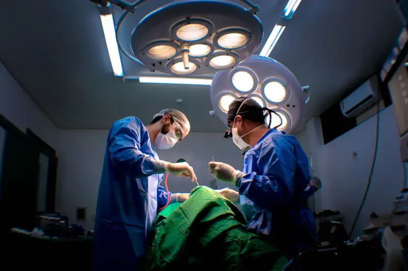 Two surgeons in gowns and headlights operating beneath round ceiling surgical lights