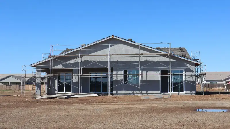 Single-story stucco house wrapped in scaffolding on a dirt lot