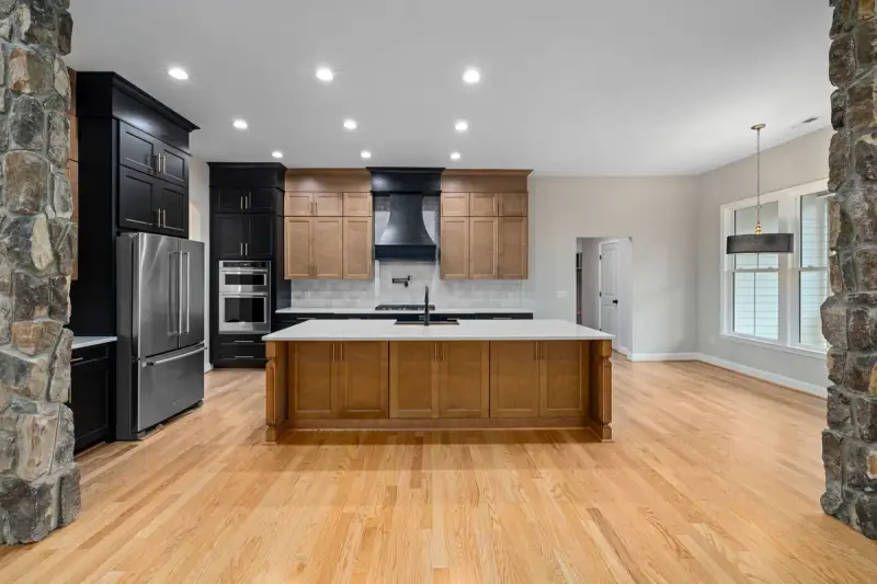 New kitchen with wood and black shaker cabinets, a large island, stone walls and hardwood floor