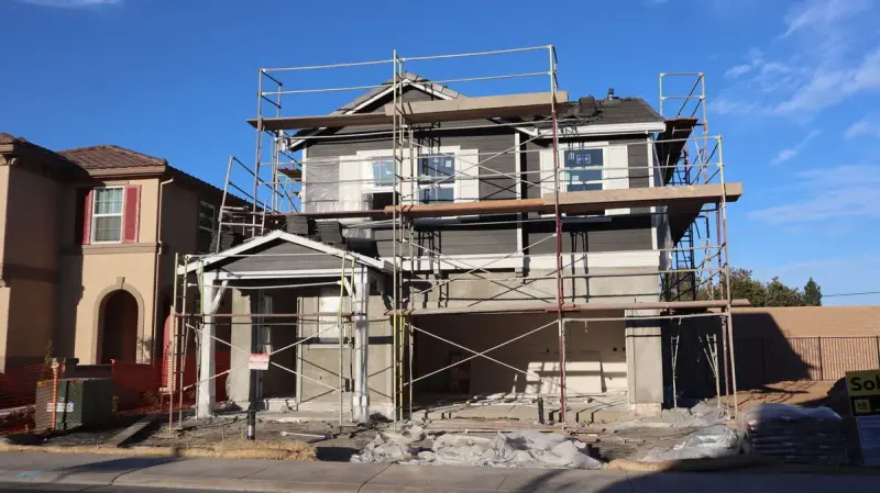 Two-story house in scaffolding between finished homes on a sunny street