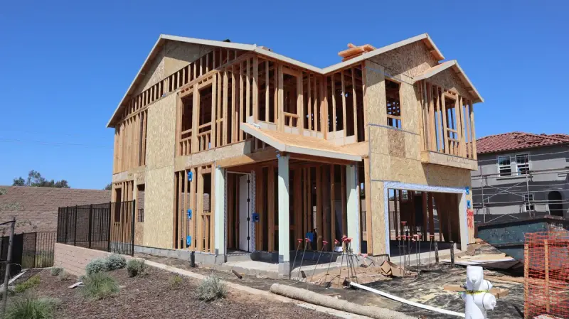 Two-story framed house with OSB sheathing, porch posts and a black fence on a new street