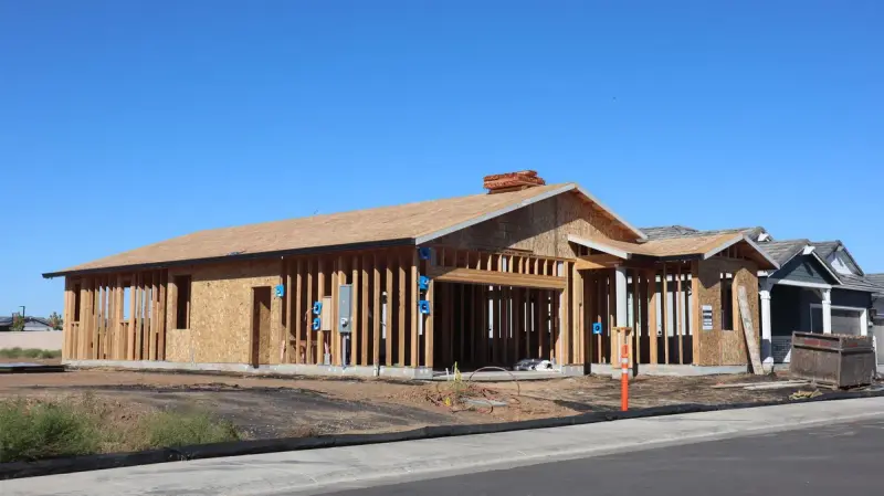Single-story framed house with roof sheathing and a brick chimney on a new street