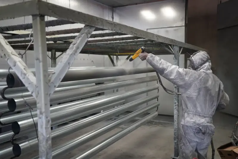 Technician in a protective suit spraying powder coating onto racked metal pipes