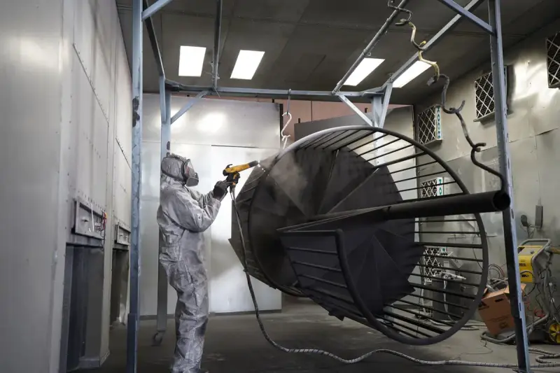 Coating technician spraying a large hanging metal frame in a finishing booth