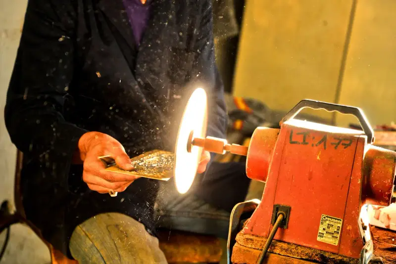 Hands holding a metal piece against a spinning polishing wheel on an orange bench grinder