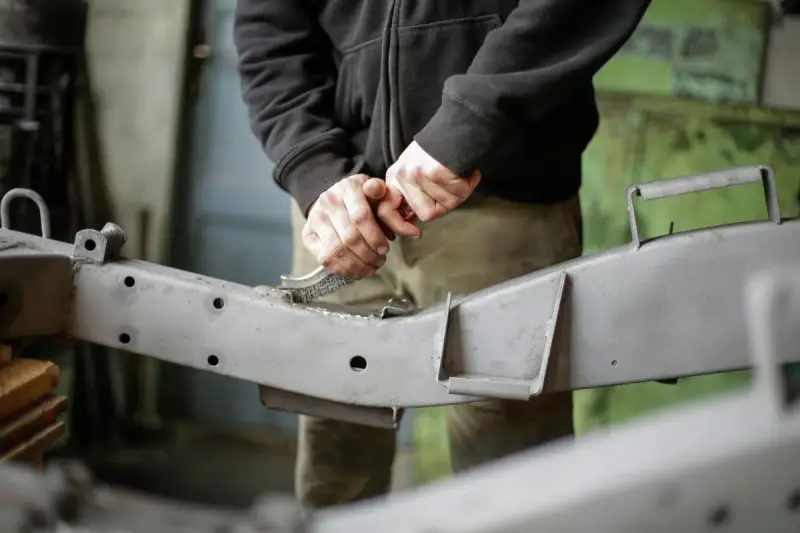 Worker scrubbing a bare steel bracket with a wire brush to prepare the surface