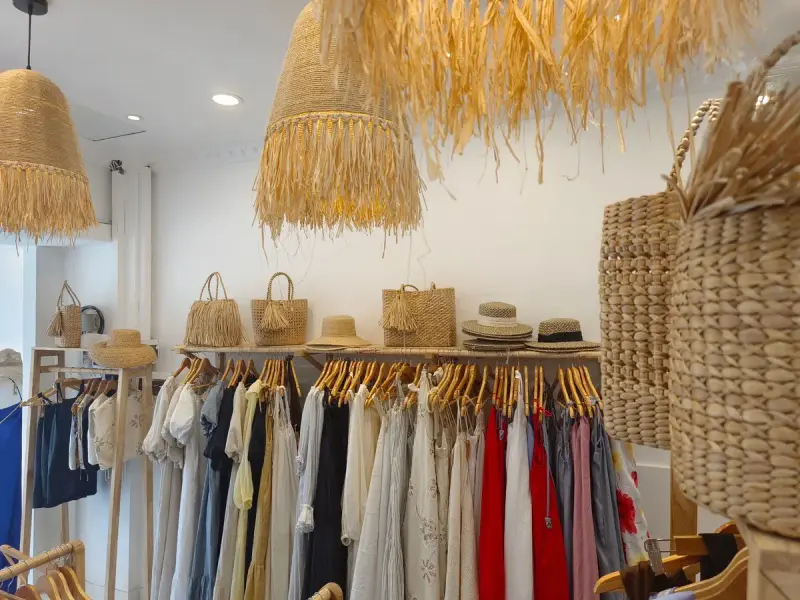 Coastal boutique with linen dresses on rails, straw bags and woven pendant lamps