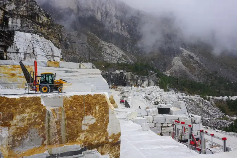 Marble quarry bench with cut faces, machinery and misty mountains behind