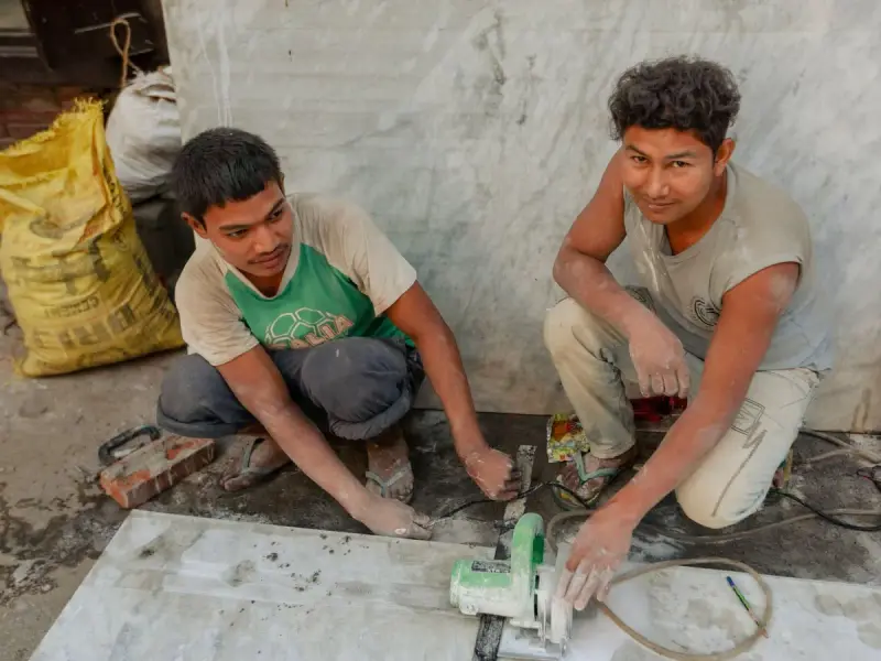 Two workers cutting a marble slab on the floor with a handheld saw