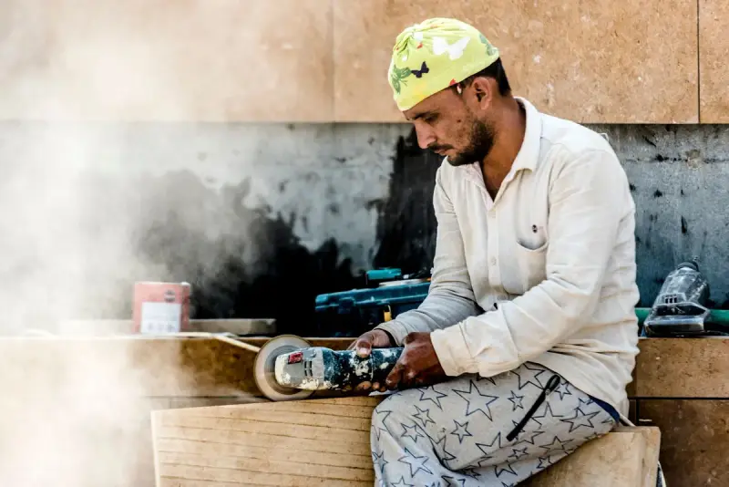 Craftsman with an angle grinder shaping stone in a dusty workshop