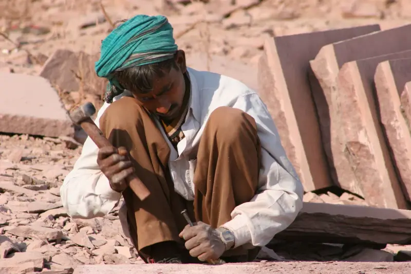 Stonemason chiseling a sandstone slab beside a stack of cut slabs