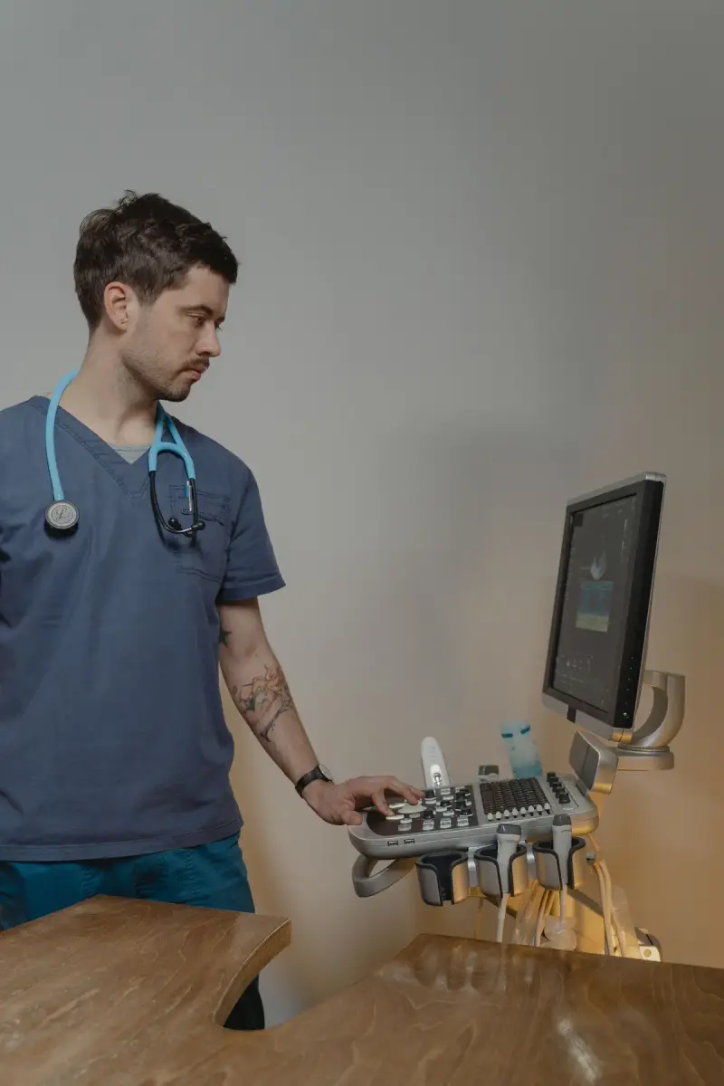 Clinician in navy scrubs with a stethoscope adjusts the controls of an ultrasound console