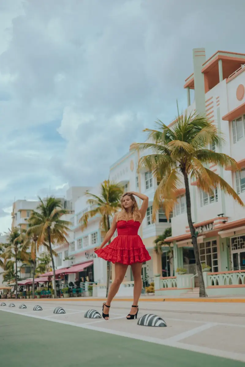 Woman in a red tiered sundress posing on an Art Deco street lined with palm trees