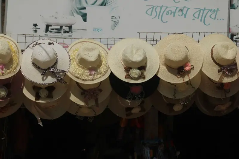 Straw hats with floral trims hanging in an outdoor market display