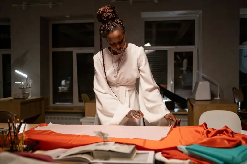 A fashion designer works on a dress at a table in her studio