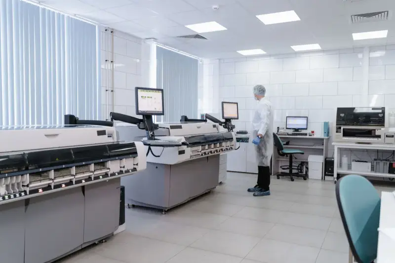 Scientist standing in a modern laboratory reviewing data on screens beside lab instruments