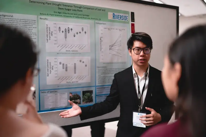 Researcher presenting plant drought tolerance findings beside a conference poster
