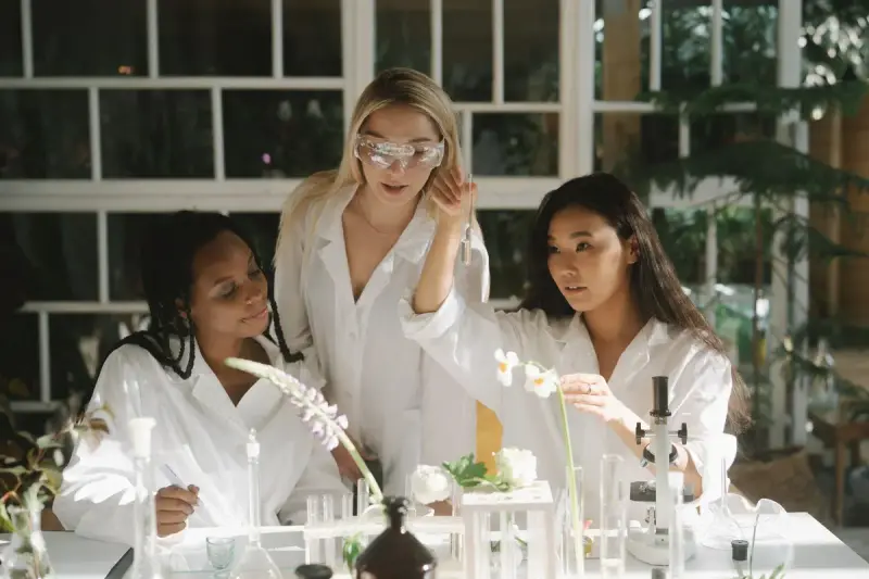 Three women scientists examining plant samples in a bright greenhouse lab