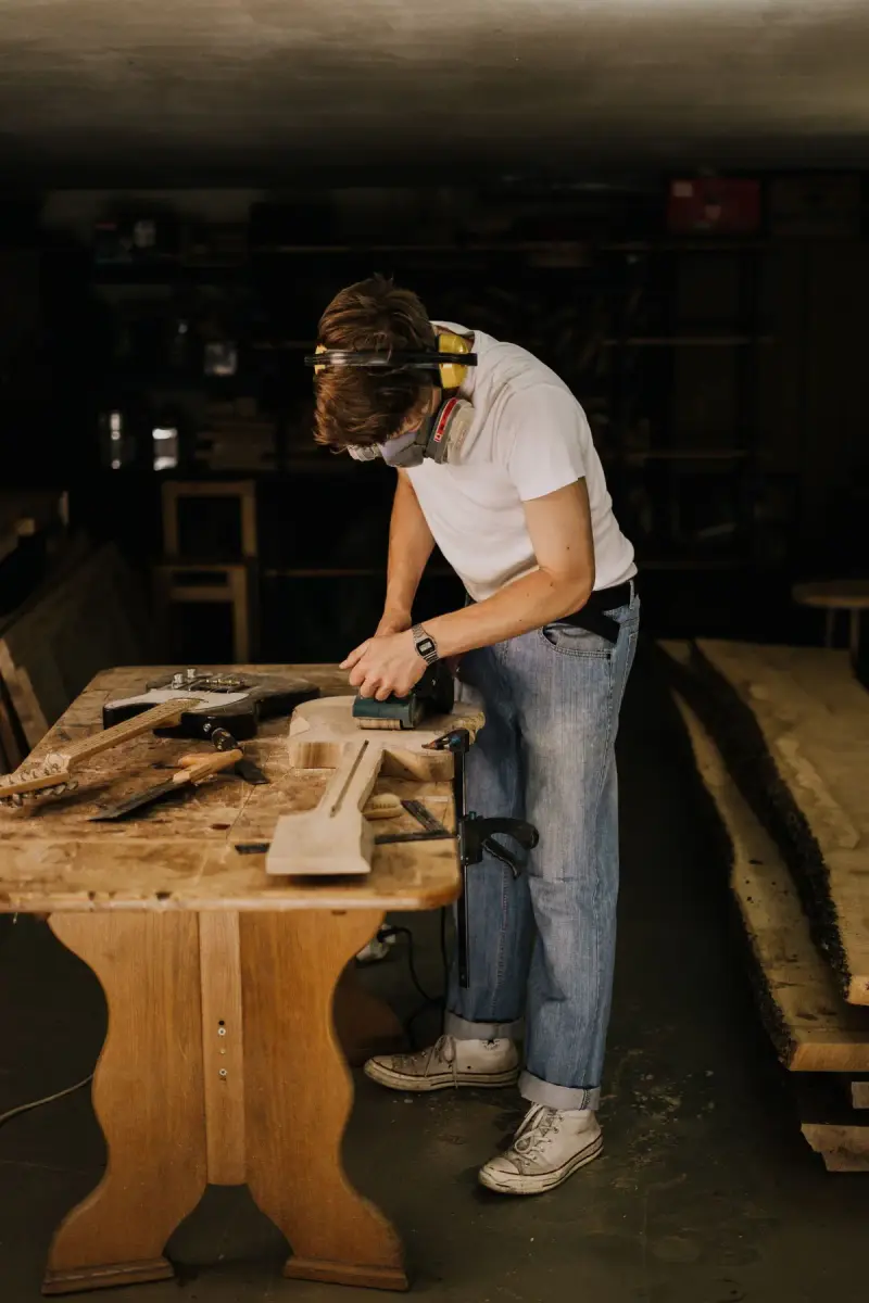 Craftsman sanding a wooden plank in a workshop wearing safety gear