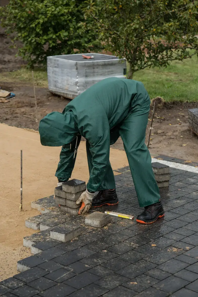 Man in rain gear laying pavers outdoors