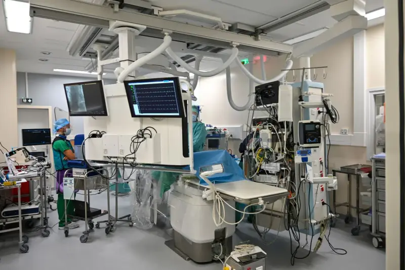 Hybrid catheterization lab with ceiling-mounted imaging arm, monitors and staff in scrubs