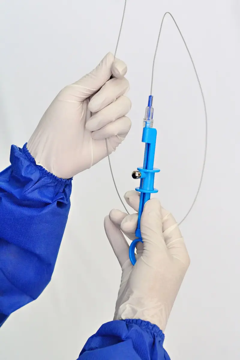 Gloved hands holding a blue catheter introducer with a thin guidewire looped above