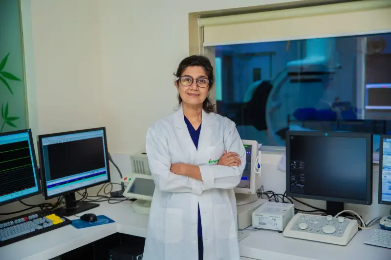 Woman physician in a white coat standing in an imaging control room beside monitors