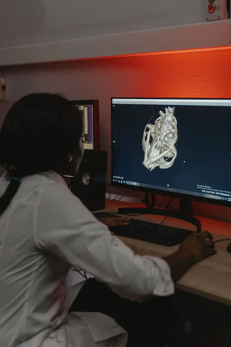 Clinician in a white coat studying a 3D scan reconstruction on a desktop monitor