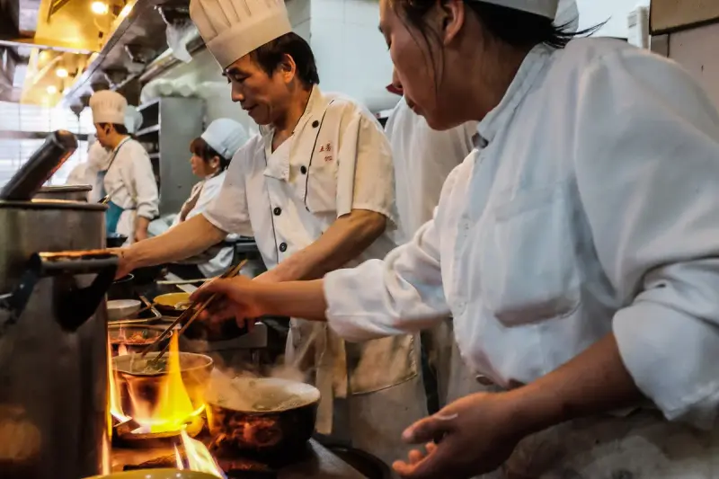 Kitchen brigade of men and women cooking over gas flames in a restaurant kitchen