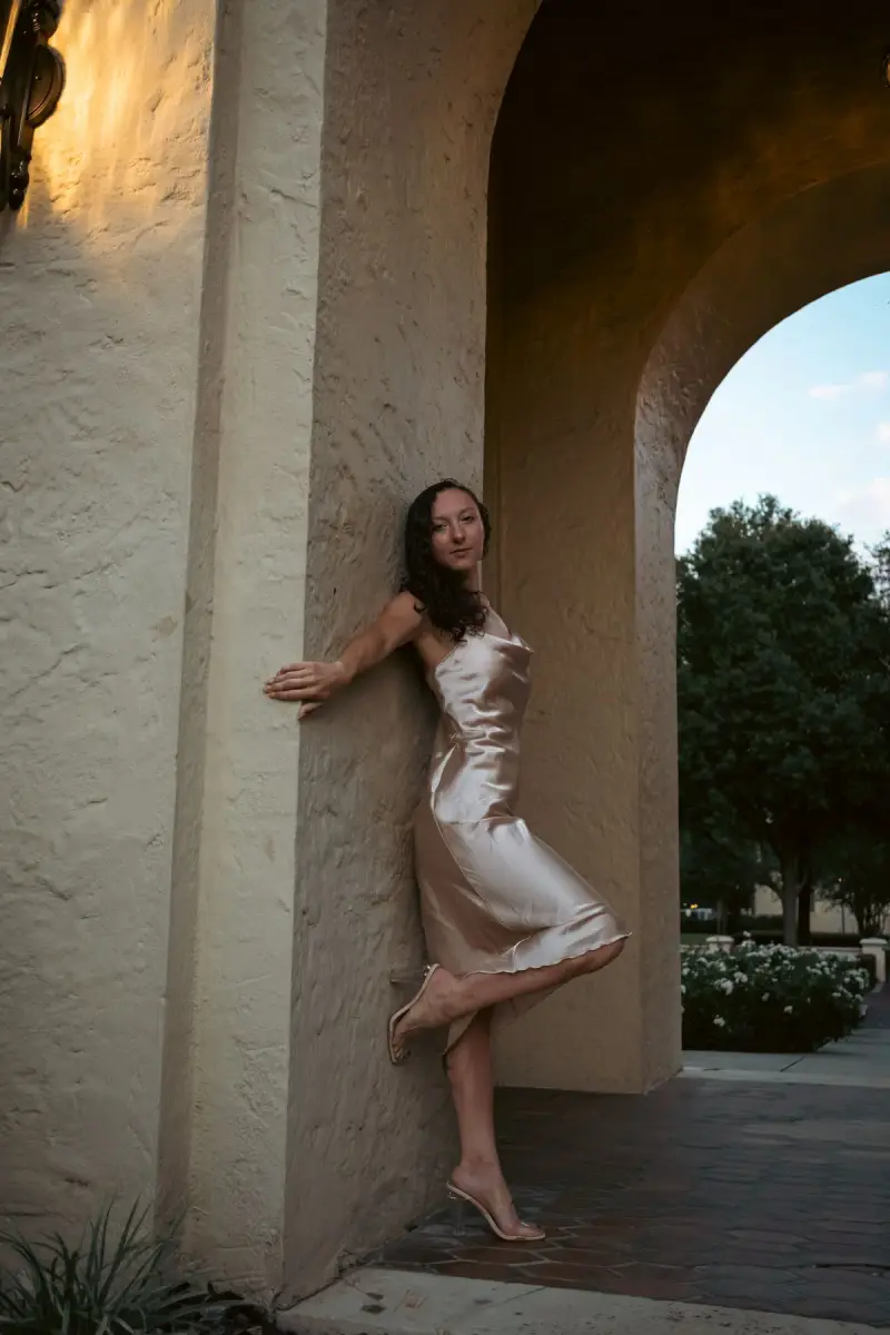 Woman in a champagne silk slip dress leaning on a sunlit stucco arch