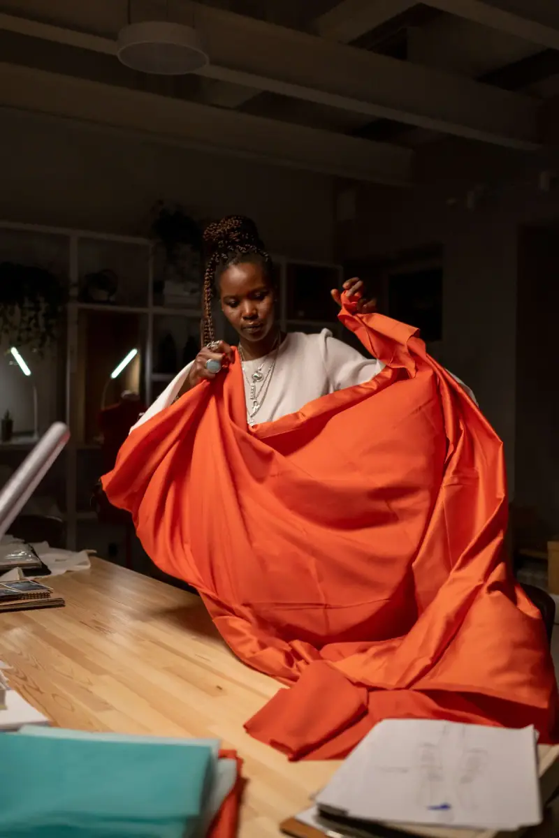 Designer holding a wide length of orange fabric over a work table