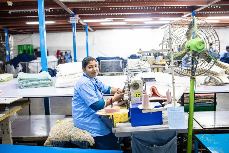 A textile worker sews fabric at a machine in a bright, organized factory