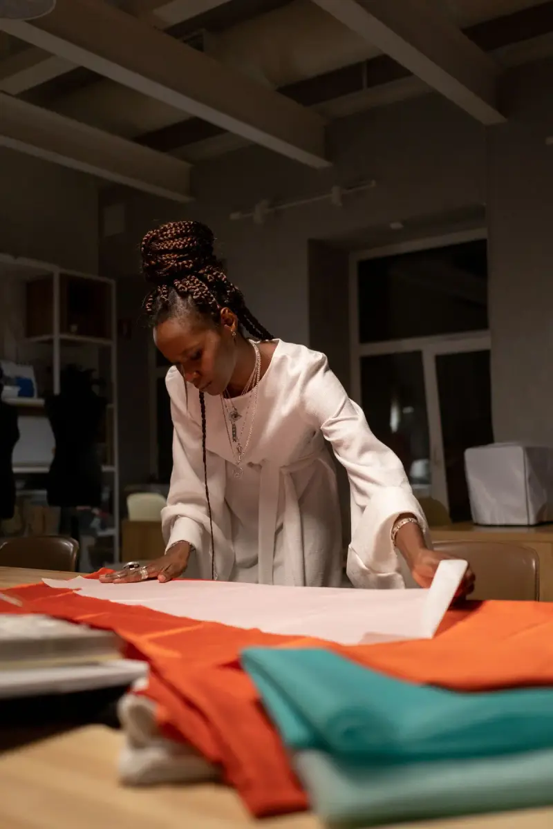 Fashion designer in a cream dress laying pattern paper on orange fabric