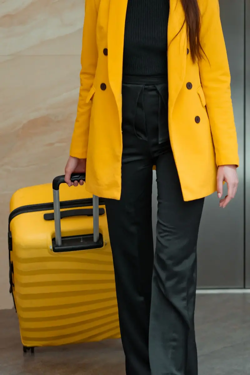 Woman in a yellow blazer and black trousers pulling a ribbed yellow hard-shell suitcase