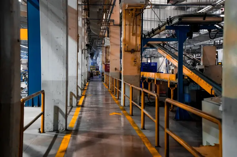 Long factory aisle with yellow railings beside inclined conveyors and assembly equipment