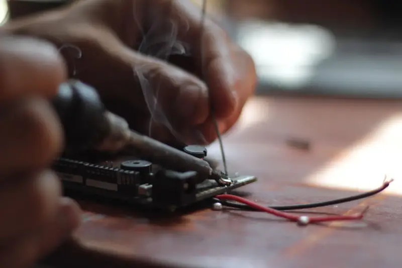Close view of a soldering iron joining a wire to a circuit board as a wisp of smoke rises