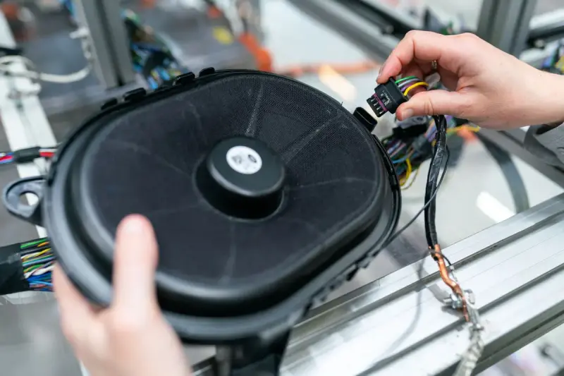 Engineer's hands connecting a wiring harness plug to a car speaker at an aluminum test bench