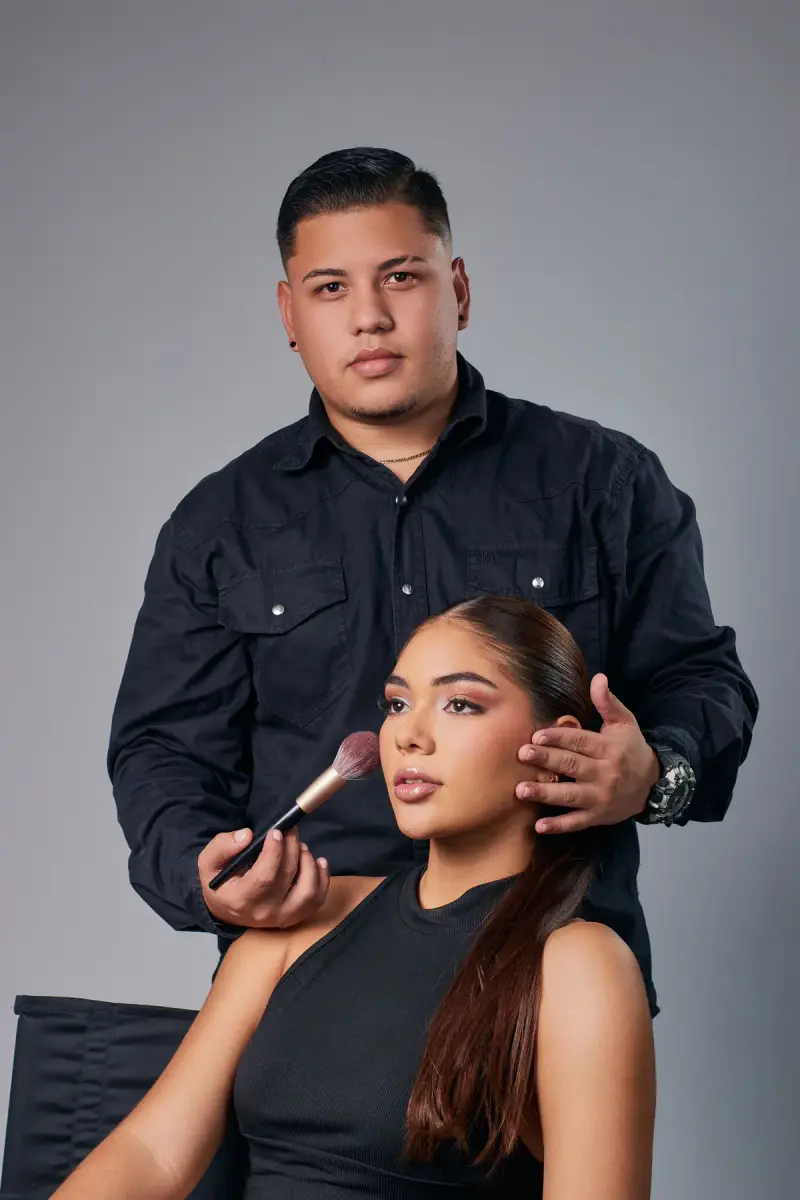 Makeup artist applying blush with a brush to a seated model in a studio