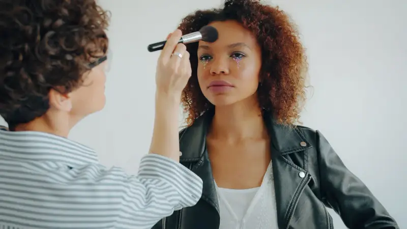 Makeup artist sweeping powder across a model's brow in a bright studio