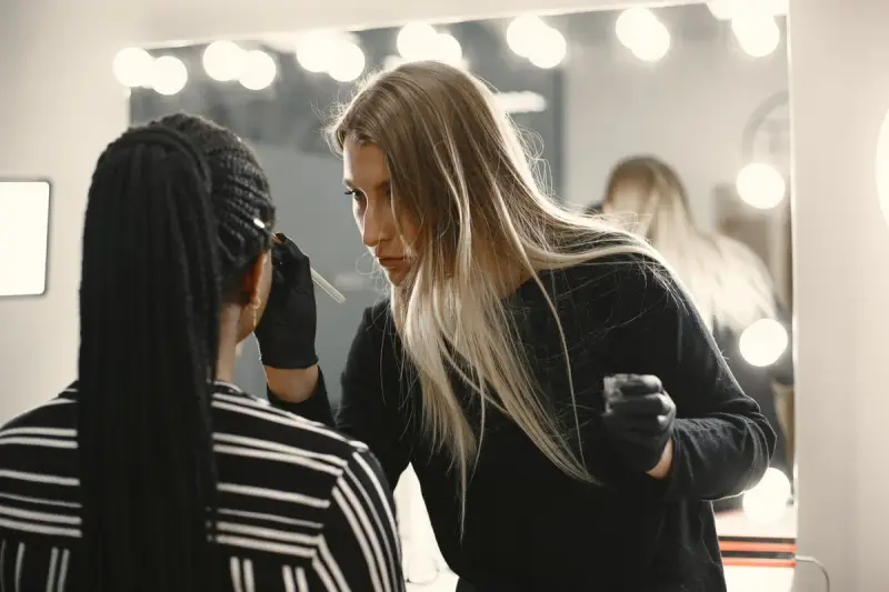 Makeup artist in gloves working on a client at a lit vanity mirror