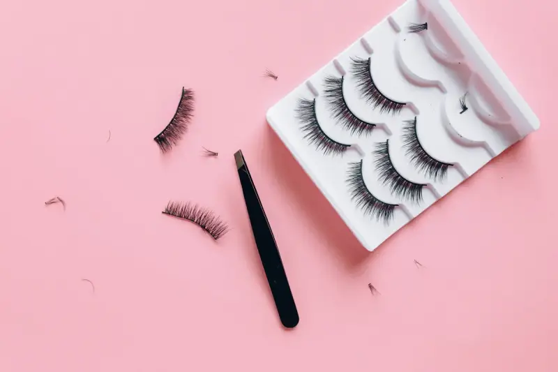 False eyelash strips and tweezers arranged on a pink background