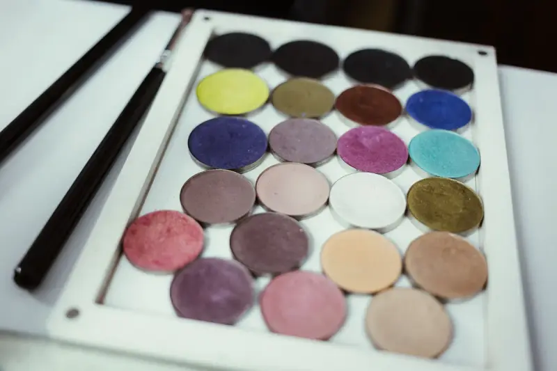 Magnetic palette of eyeshadow pans in purples, greens and neutrals with two brushes