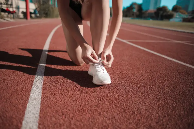 Runner tying a white sneaker on a red running track