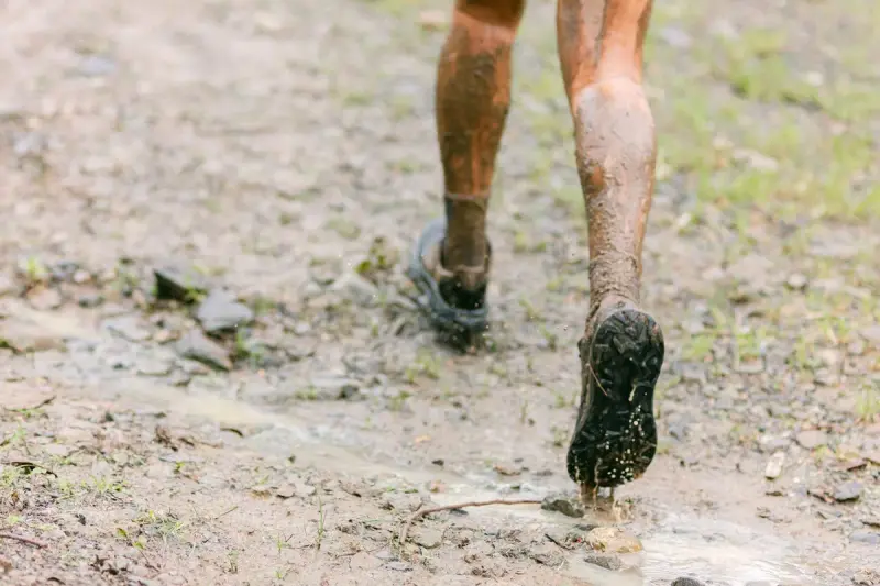 Mud-splashed legs and trail shoes striding along a wet dirt path