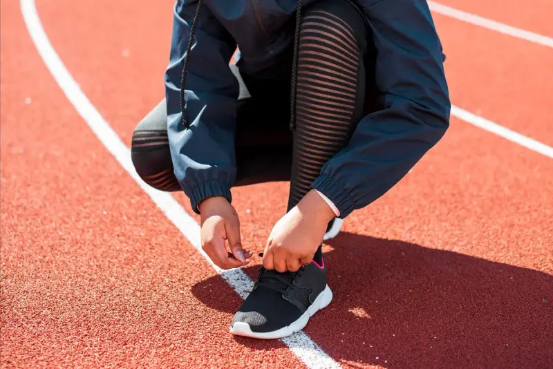 Athlete in a dark jacket tying running shoes on a track lane